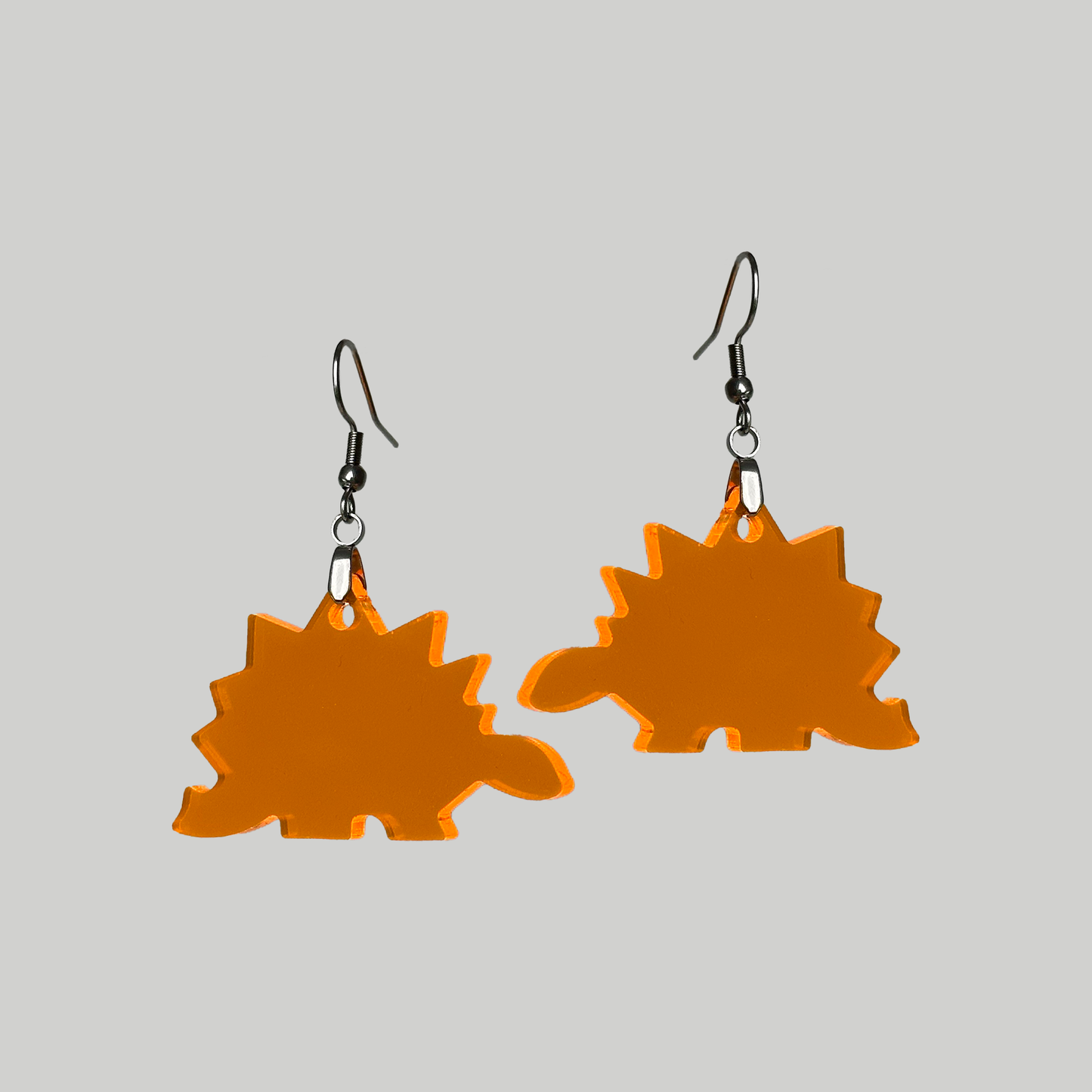Earrings shaped like a stegosaurus dinosaur, designed in fluorescent orange for a vibrant and standout look everywhere.